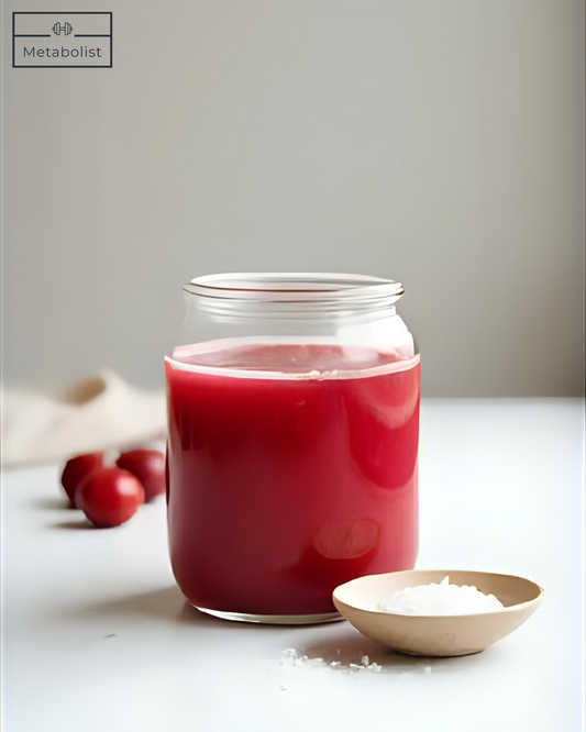 Jar of red liquid with apples and a bowl on a light surface, featuring the brand 'Metabolist'.
