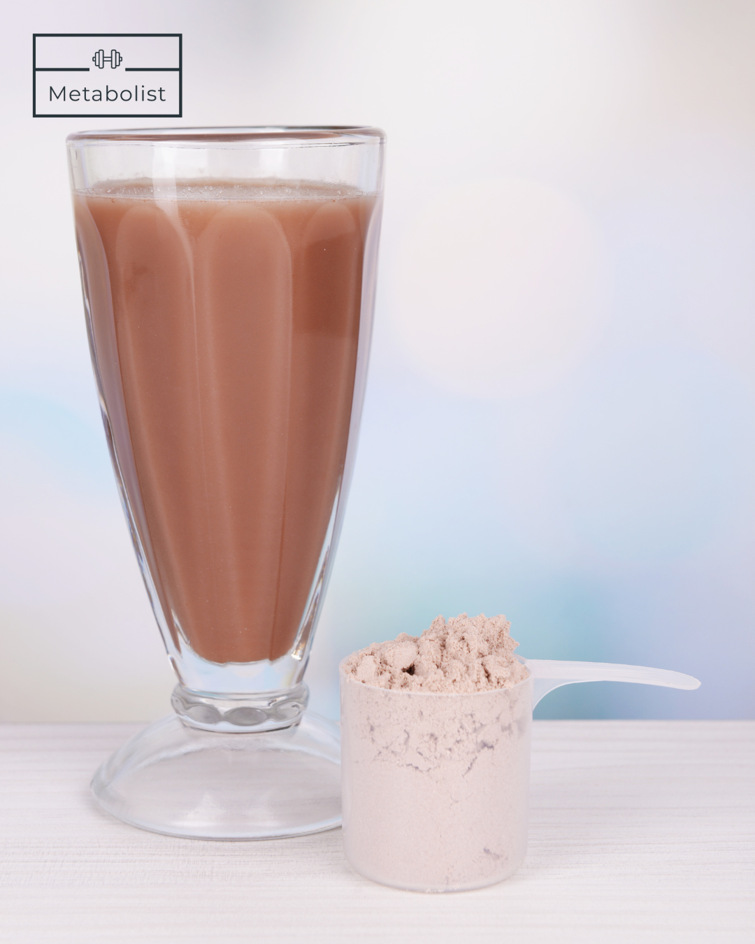 Glass of chocolate milkshake with a scoop of protein powder on a white background, featuring the 'Metabolist' brand.