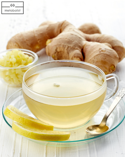 Glass teacup with ginger tea, sliced ginger, and whole ginger root on a white surface.