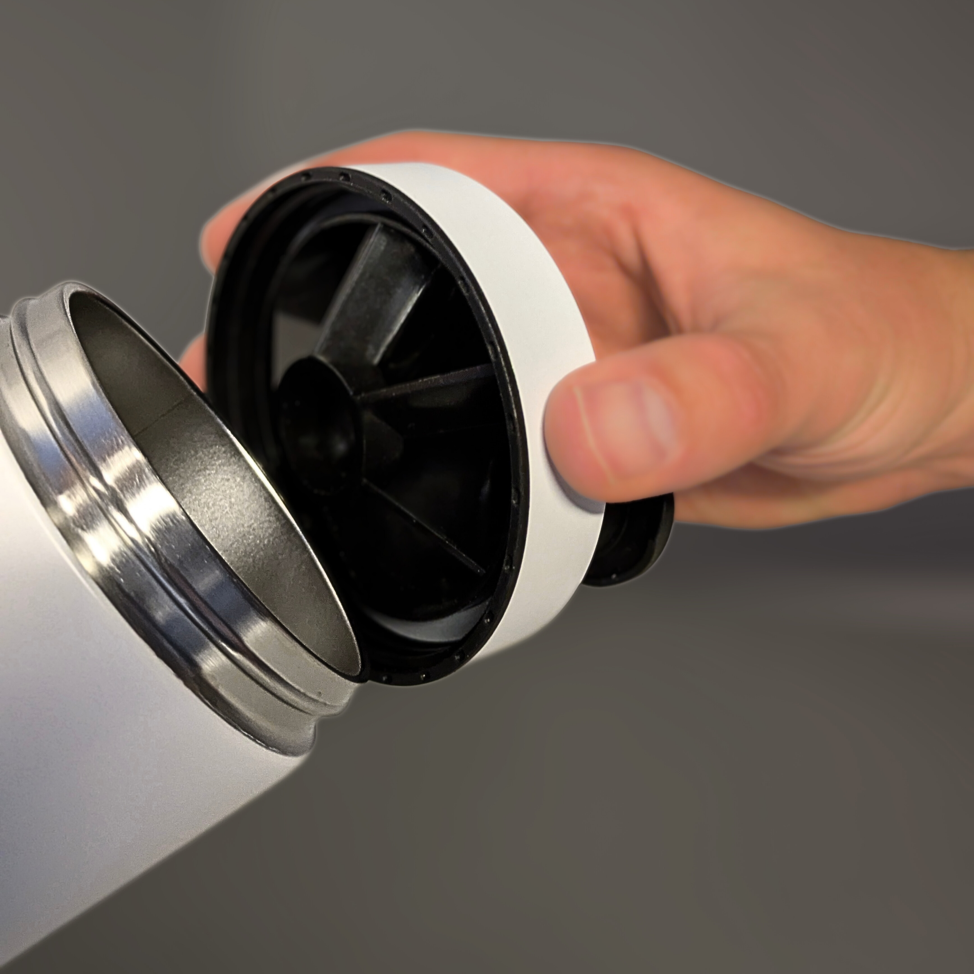 Hand holding a white and black lid of a Metabolist Premium stainless Steel Precision Shaker Bottle against a gray background. Metabolist Premium Stainless Steel Precision Shaker Bottle