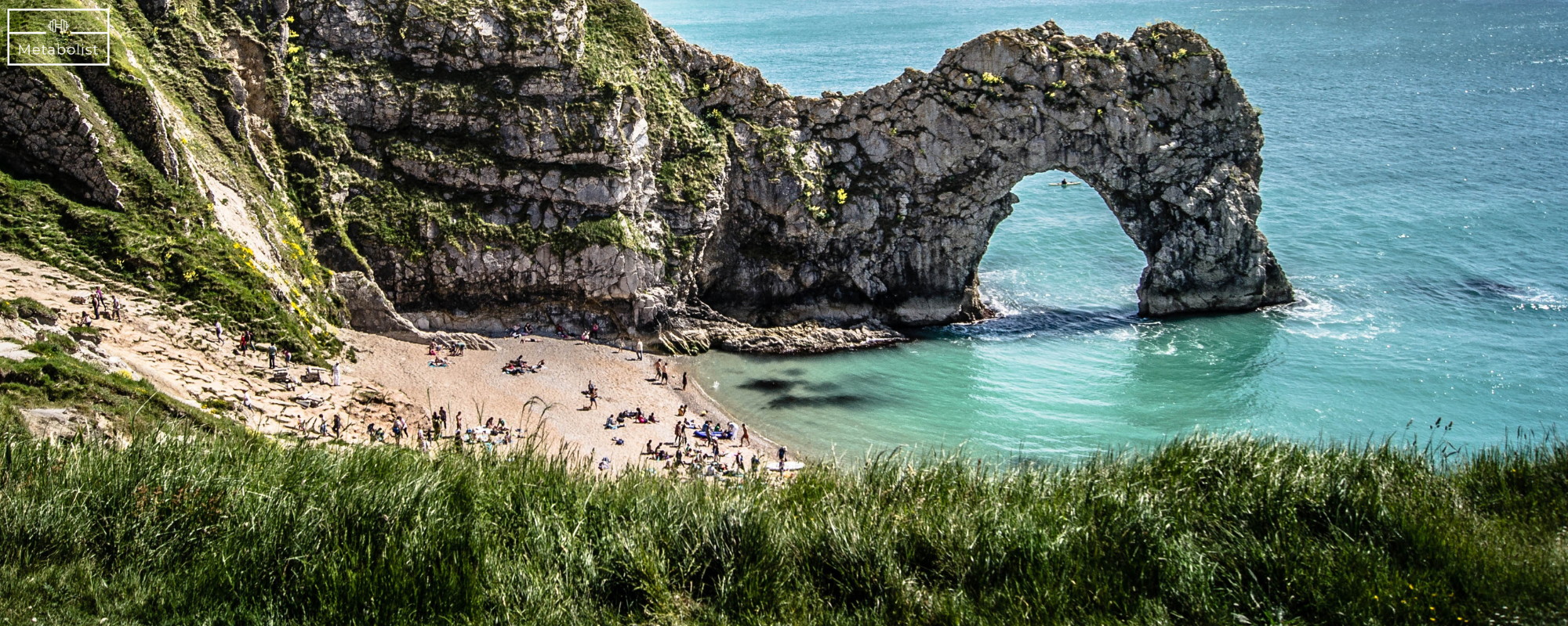 Cave formation in a coastal landscape with people on a beach.